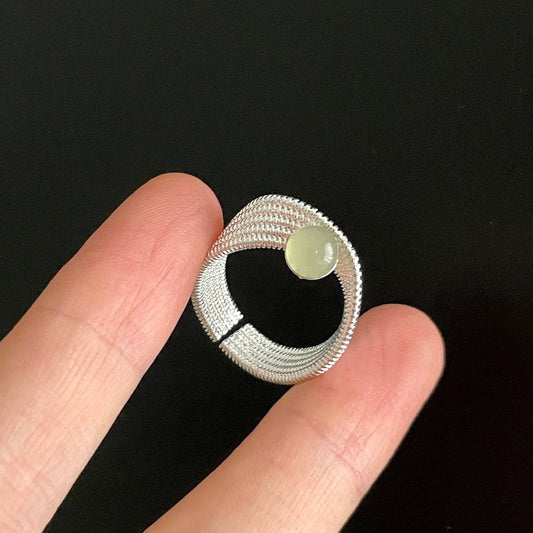 Silver coil with a green stone held between fingers against a black background