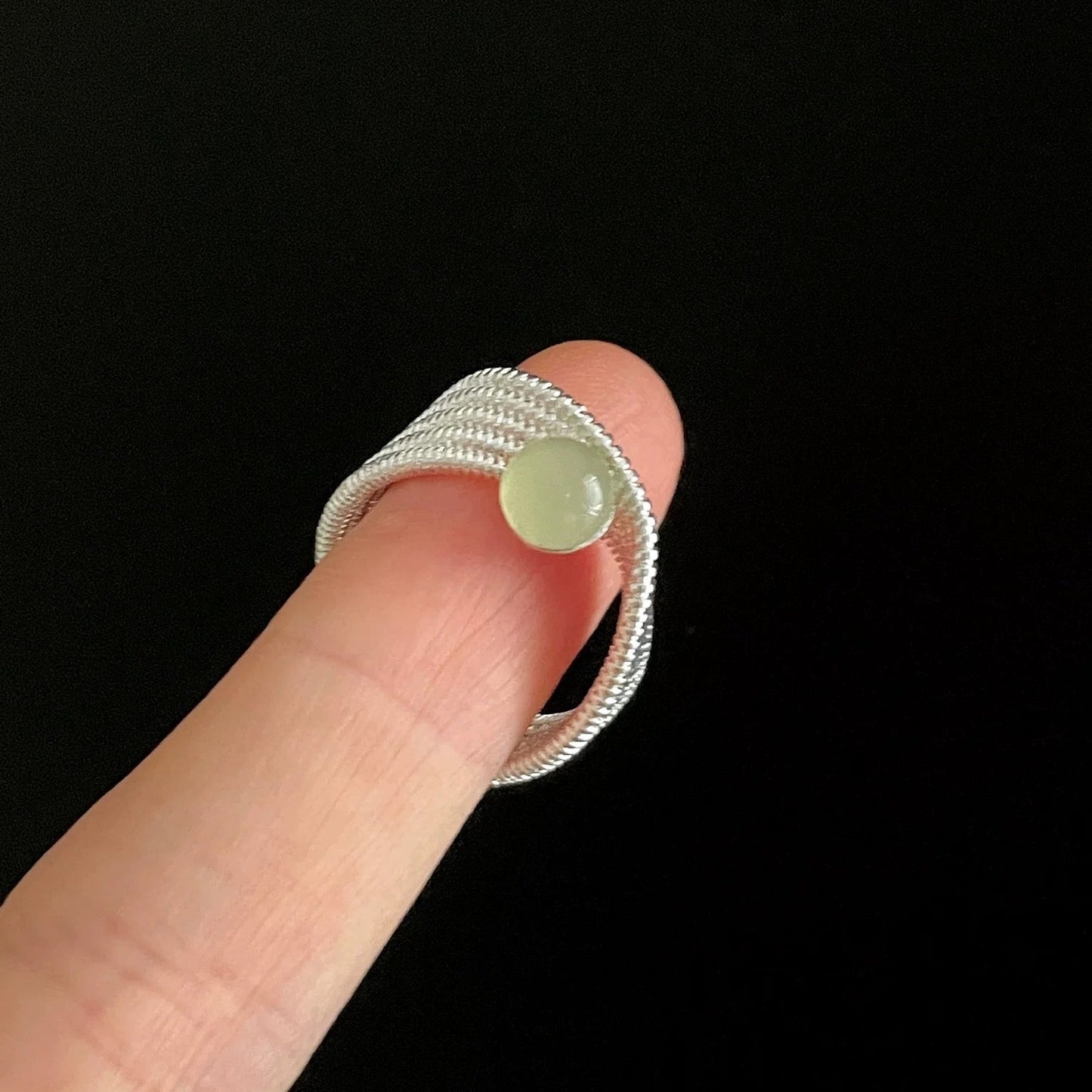Silver ring with a green stone on a finger against a black background