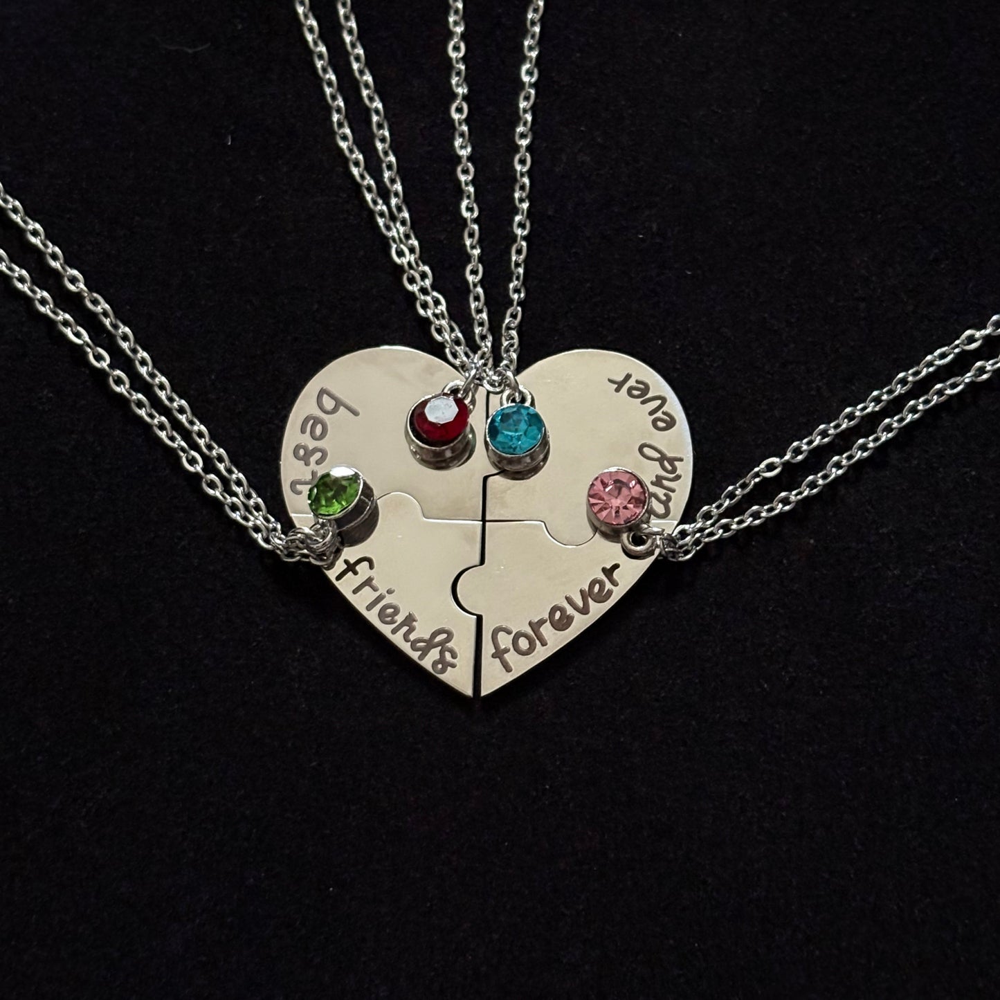 Heart-shaped pendant with engraved text and colorful gemstones on a black background
