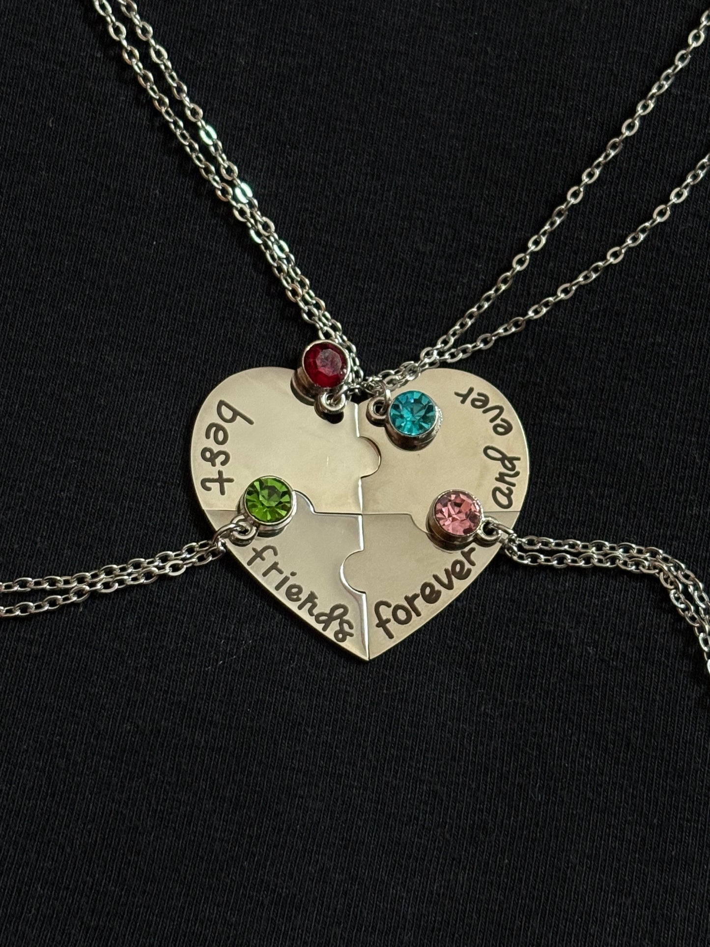 Silver heart-shaped puzzle piece necklace with engraved text and colored stones on a black background