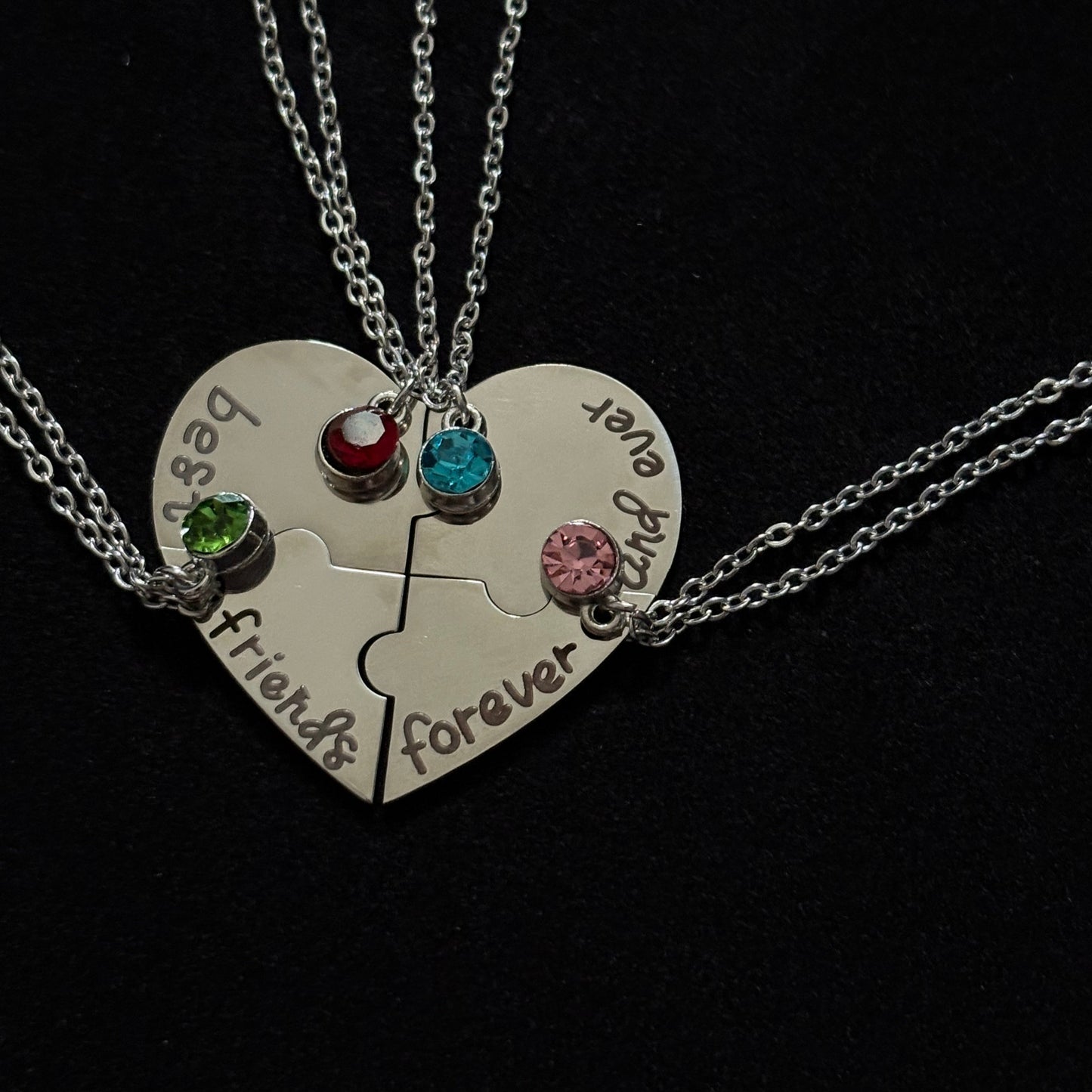 Heart-shaped split necklace with engraved text and colored stones on a black background