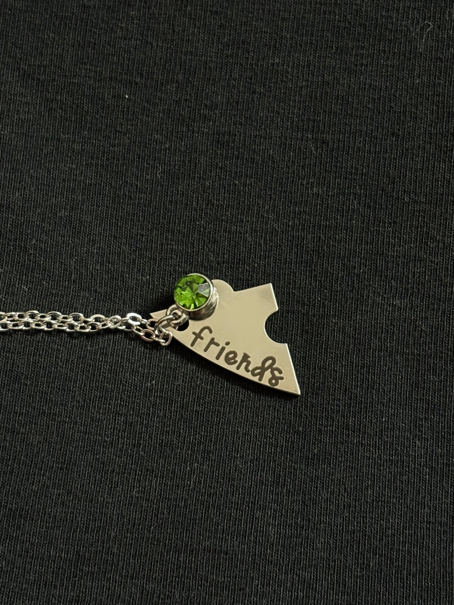 Silver necklace with a pendant shaped like a state and 'friends' engraved, on a dark background