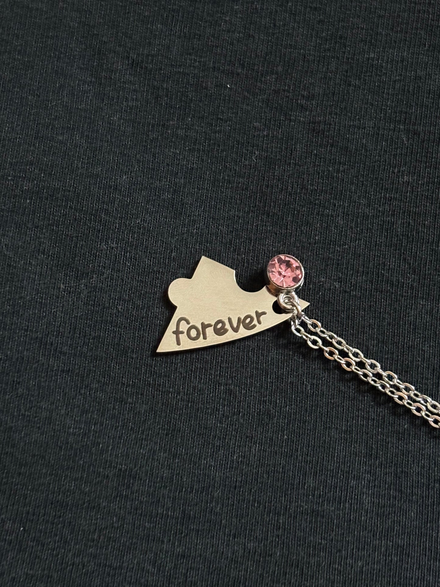 Necklace with a heart-shaped pendant and pink charm on a black background