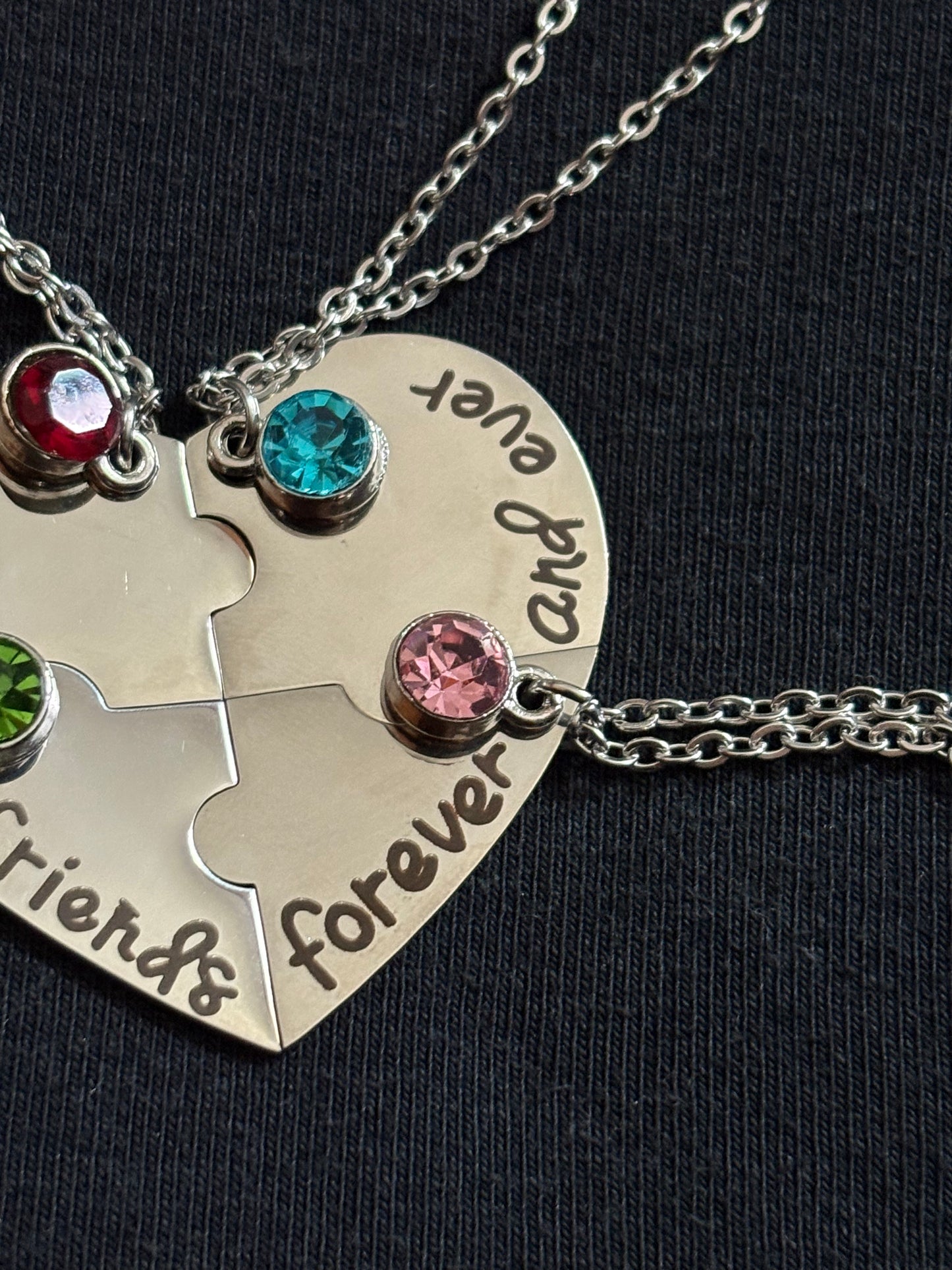 Silver necklace with puzzle piece pendant and colored gemstones on a black background