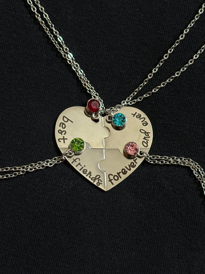 Silver heart-shaped puzzle piece necklace with engraved text and colored stones on a black background