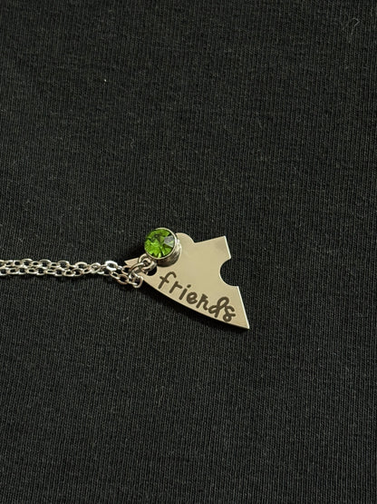 Silver necklace with a pendant shaped like a state and 'friends' engraved, on a dark background