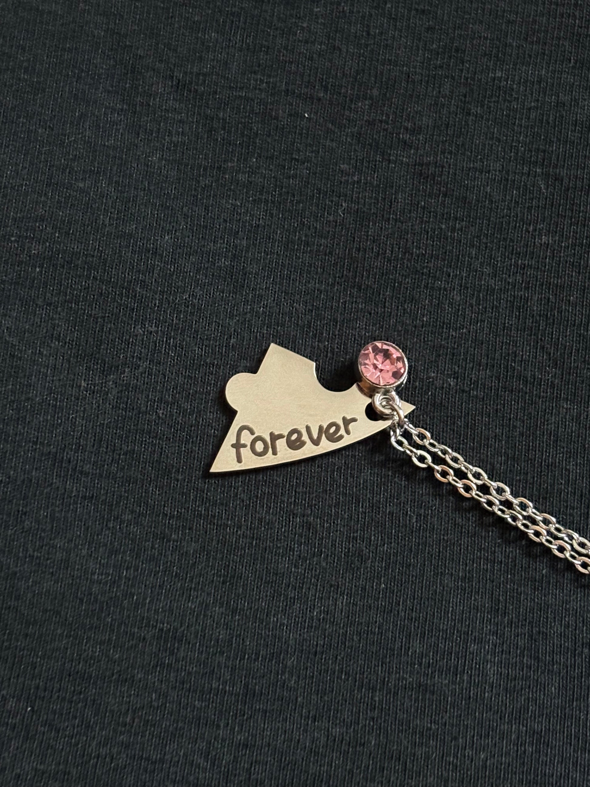Necklace with a heart-shaped pendant and pink charm on a black background