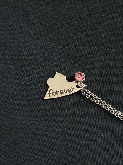 Necklace with a heart-shaped pendant and pink charm on a black background