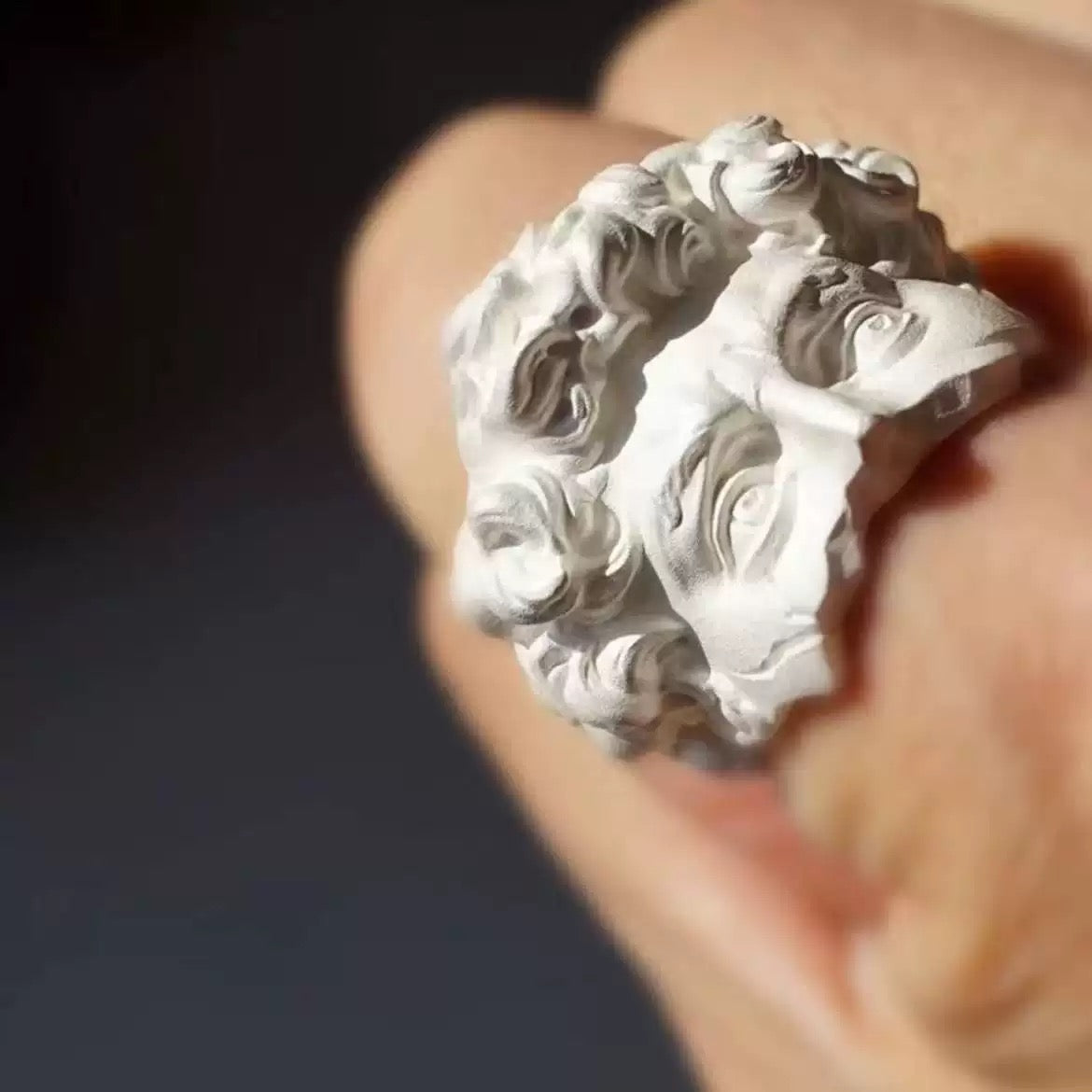 Silver ring with intricate design held by a hand against a dark background