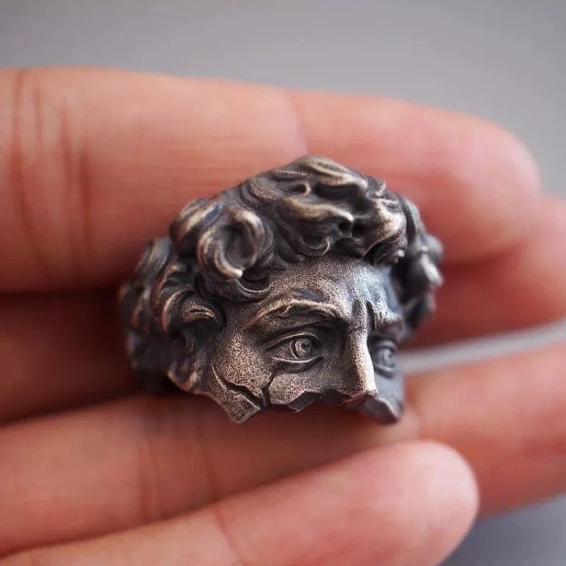 Silver ring with detailed design held in a hand against a neutral background